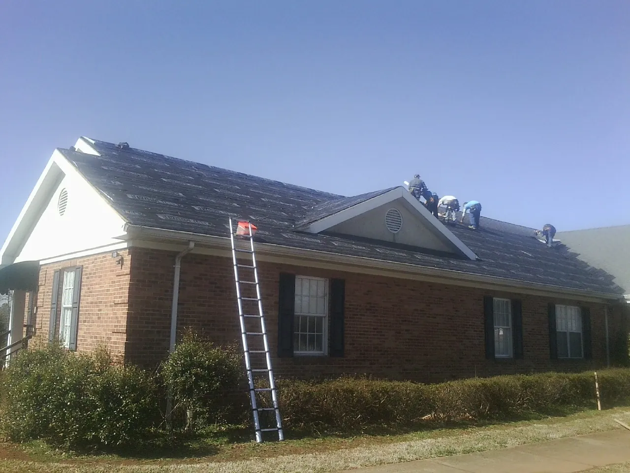 Crew tearing shingles off a brick ranch roof with a ladder set — Emergency Roof Repair work by our crew in Montgomery